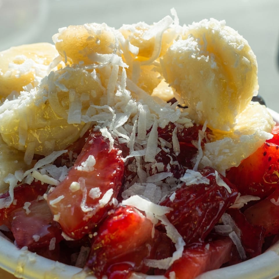 Strawberries and banana pieces topped with shredded coconut and powdered sugar in a bowl.